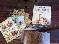 Photo showing vintage and modern cookbooks scattered alongside wooden salad bowl with utensils and fermentation kit box