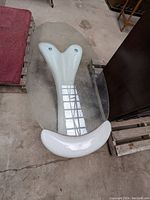 Top view of oval glass table with white sculptural plastic base, showing glass top and base shape.
