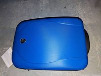 Top view of the closed blue hard shell suitcase showing its smooth exterior surface with black edging and brand emblem.