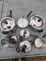 Full view of 14 piece Lagostina cookware set with pots, pans, and lids arranged on metal surface.