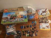 Photo showing the LEGO Minecraft Crafting Box with pieces in a plastic bag, two LEGO Creator 3-in-1 boxes with instruction booklets and loose pieces, and laid out minifigures from multiple franchises.