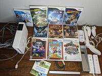 Photo showing the Nintendo Wii console with 10 Wii game cases, two Wii controllers with shooting extensions, sensor bar, and cables.