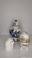 Photo of the three porcelain items together: Blue Delft jar with lid, floral egg trinket box with hinged lid, and small white swan figurine.