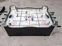 Top angle showing entire table hockey game surface with players, rods, and goals. Black base under the playing surface. No legs attached.