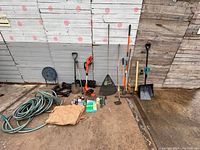 Wide view of all yard tools and garden accessories arranged on ground against wooden wall