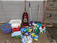Full overview of lot items set on floor showing vacuum, brooms, Swiffer Wet Jet, laundry baskets, bucket, and cleaning supplies