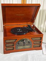 Wooden cabinet turntable with hinged lid open revealing turntable and tonearm, front side view showing speaker grills and Crosley branding