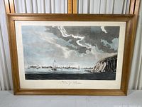 Full view of the framed print showing Boston Harbor with ships and the town in the distance, wooden frame and beige mat visible.