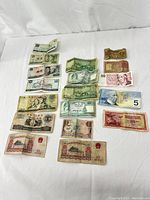 Top-down image of all foreign currency notes arranged roughly in rows on a white surface showing wear and folds on notes.