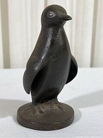 Front view of bronze penguin figurine standing upright on round base.
