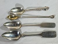 Four pieces of silver flatware including two spoons and two spreader knives shown for overall view.