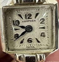 Close-up of square silver-tone dial showing Arabic numerals, blued hands, 'Hampden Swiss' marking