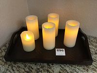 Six ivory colored battery operated candles of varying heights placed on a dark wooden tray. Candles show lit flame effect.