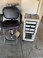 Side-by-side photo of the black hydraulic salon chair next to the white salon cart showing general condition and setup.