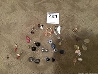 Top-down view of 19 costume earrings of various styles and colors spread on carpet showing diversity in hoops, studs, and dangles.