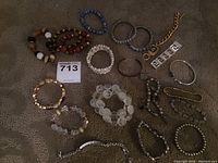 Overview of 15 various costume jewelry bracelets displayed on a textured surface, showing different styles including beaded, chain, and elastic bands.