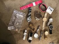 Shows assortment of 12 watches and accessories including pink and black watches, metal and plastic bands, with watch components in a plastic bag.