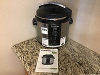 Front view of the Cuisinart electric pressure cooker sitting on a granite countertop with the user manual placed in front.