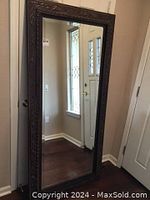 Full view of tall decorative mirror with dark bronze frame and beveled glass, standing on floor near doorway.