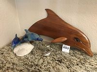 Large wooden dolphin carving and ceramic dolphin pair sculpture on granite counter.