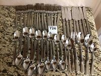 Full set of stainless steel forks, knives, tablespoons, and teaspoons arranged on a granite countertop.