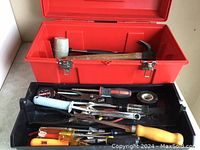 Photo of open red toolbox showing multiple hand tools inside including hammers, screwdrivers, pliers, caulking gun, electrical tape and other small tools.