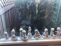 Eight Jonathan & David Precious Moments collectible porcelain figurines arranged on a windowsill with greenery background.