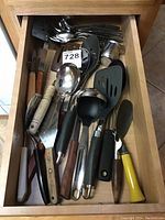 Top view of a drawer filled with assorted kitchen gadgets including spatulas, spoons, knives, and ladles with various handle types and sizes