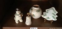 Wide view showing all four pieces in the collection arranged on a shelf: snowman figurine, bell, globe vase, and tree-shaped dish on stand