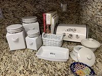 Overview of the lot on granite countertop showing canisters, casserole dishes, bread box, cookbooks, and decorative bowl.
