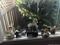 Wide shot of all four items on a windowsill including carousel horse, child with rabbit figurine, cat figurine music box, and frog planter.