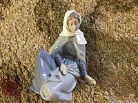 Seated maiden figurine in blue-gray and white headscarf viewed from above showing delicate hand painting and glossy finish.