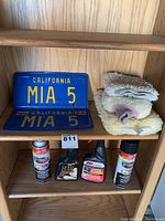 Shelf display of vintage 1986 California license plate and frame with car cleaning products and cloths on shelves.