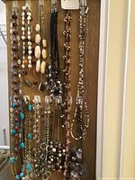 Photo showing variety of vintage costume jewelry necklaces hanging against wooden door. Includes mix of bead styles and chain styles in earth, white, gold, black and turquoise colors.