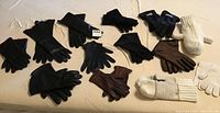 Top-down photo showing a variety of gloves and mittens in black, brown, and white, including knit and leather options.