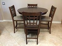 Photo shows round wooden dining table with three chairs placed around it.