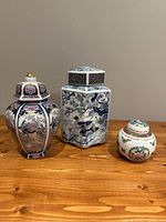 Three ginger jars of different styles and sizes shown on a wooden surface against a neutral wall
