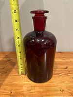 Side view of ruby red Pyrex apothecary bottle with a tape measure showing height approximately 8 inches.