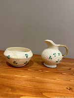 Front view of open sugar bowl and cream pitcher showing shamrock pattern and raised relief basket weave.