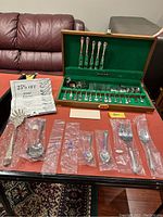 Overview of open wooden chest and all flatware pieces, bags, flyer, note and storage box laid out