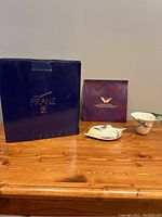 Full lot with original box, pamphlet, the porcelain cup and saucer on a wooden table