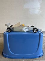 Side view of silver race car ceiling fixture with yellow helmeted driver figurine, showing aerodynamic details and tires.