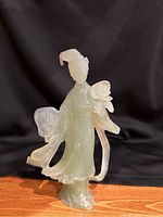Front view of vintage green jade figurine of woman holding flower and fan on wooden surface with black backdrop.