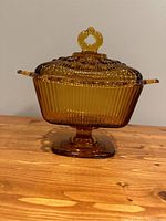 Amber Indiana Glass candy dish with lid on pedestal base shown from the front on wooden surface.