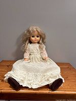 Full view of the 18-inch vintage doll seated, showcasing long white lace dress, dark shoes, and blonde hair.