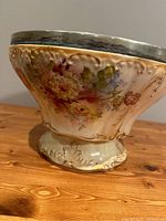 Side view showing floral relief and metal rim of the footed bowl