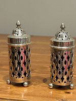 Pair of vintage sterling silver footed salt and pepper shakers with intricate cutout patterns and cobalt blue glass inserts visible through openings, photographed on a wood surface.