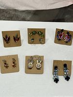 Photo of all 6 pairs of vintage multi-colored rhinestone earrings laid out on white background showing variety of styles and colors including clip-on, screw backs, and pierced closures.