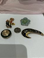 Top down view of four vintage enamel brooches arranged around a US quarter for size reference. Includes clown, flower, circle, and swoosh shapes.