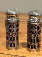 Pair of vintage silverplate salt and pepper shakers with blue cobalt glass inserts on wooden surface showing cutout design and tarnish